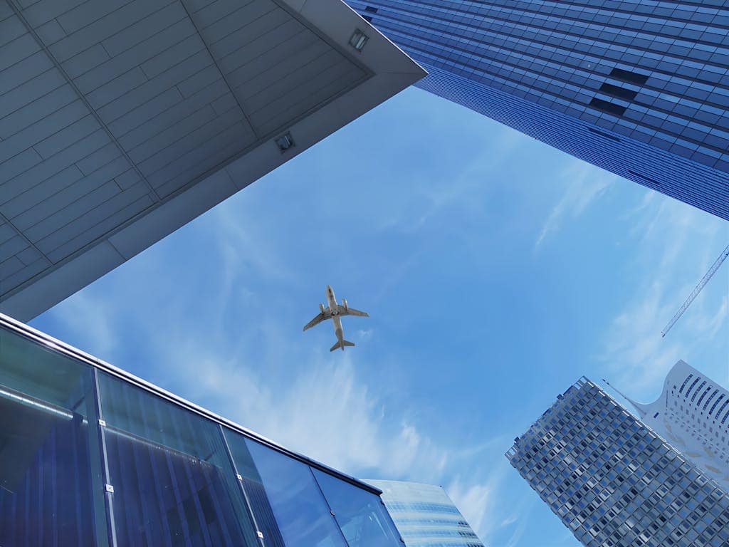 Low angle view of an airplane flying over modern skyscrapers against a blue sky in Vienna.