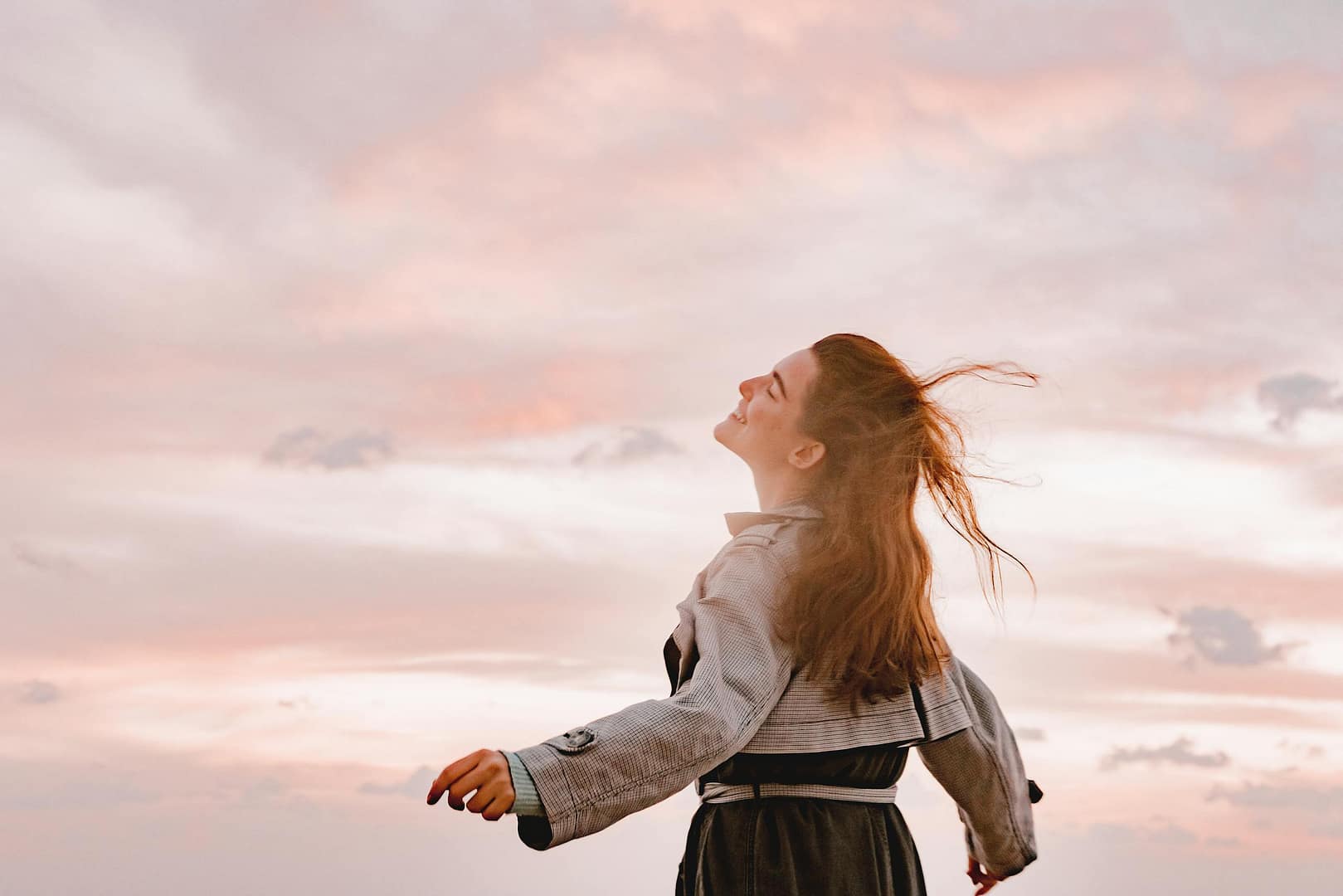 A woman joyfully embraces the sunset with arms spread in freedom, capturing serenity in nature.