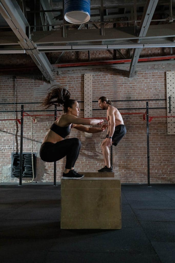 Adults performing plyo box jumps in a gym setting, focusing on fitness and strength.